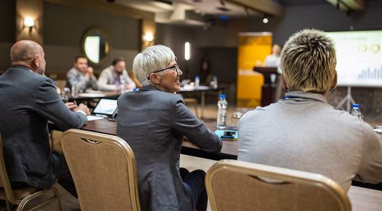 A large group of business conference participants listening to a young woman's speech in a luxury hotel's conference room