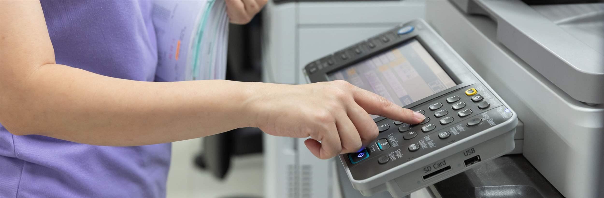 Bussinesswoman using copier machine to copy heap of paperwork in office.