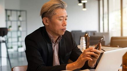 asian senior male using laptop and phone on cafe