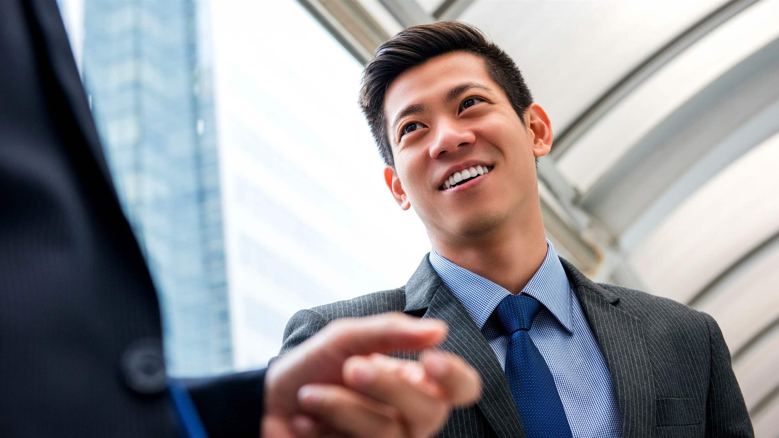 Young handsome Asian Chinese businessman talking with partner outdoors in the city