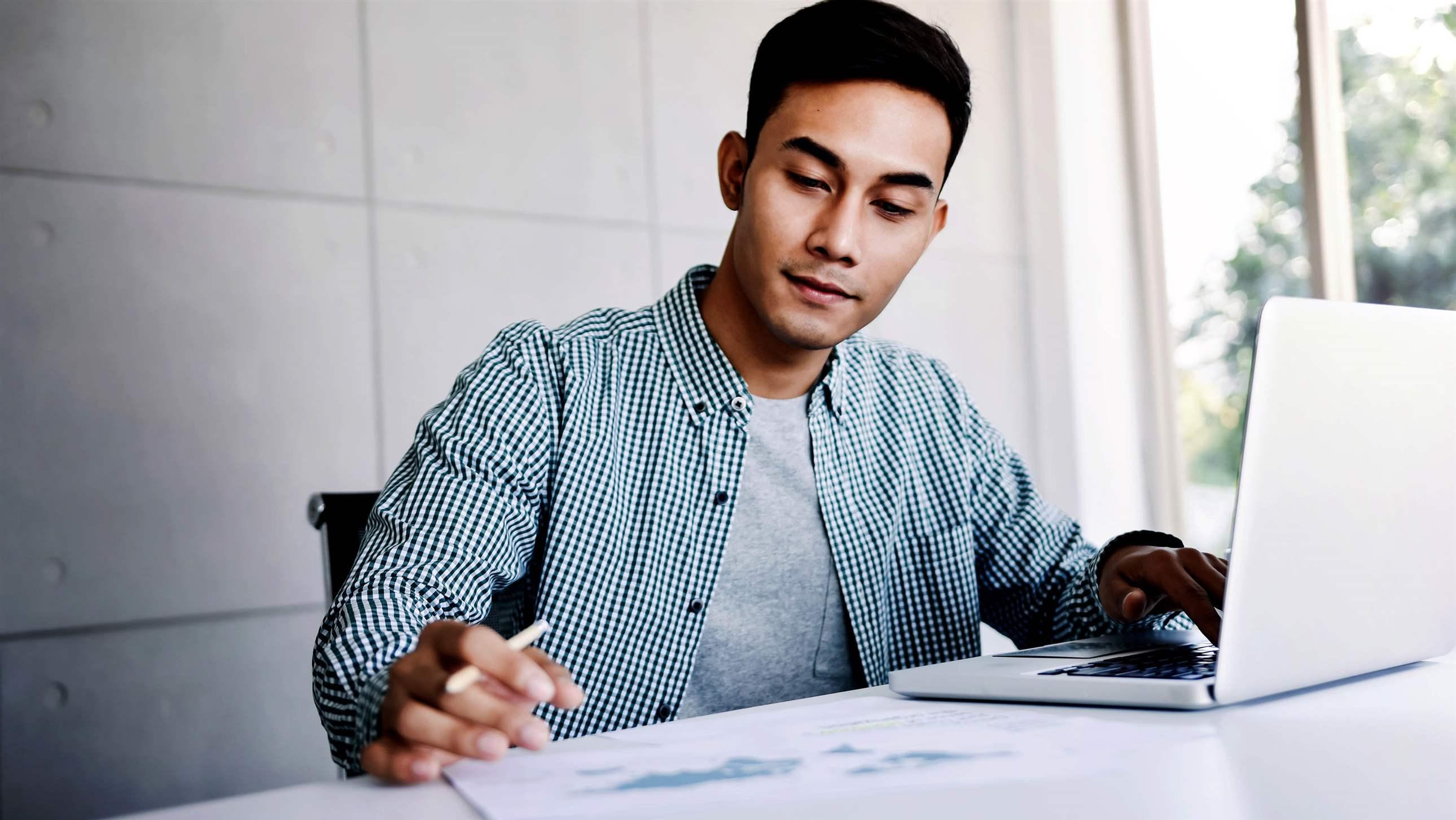Happy Young Asian Businessman Working on Computer Laptop in his Workplace