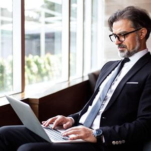 Concentrated senior businessman using laptop in lobby and examining report. Serious manager immersed in work out of office. Technology in business concept