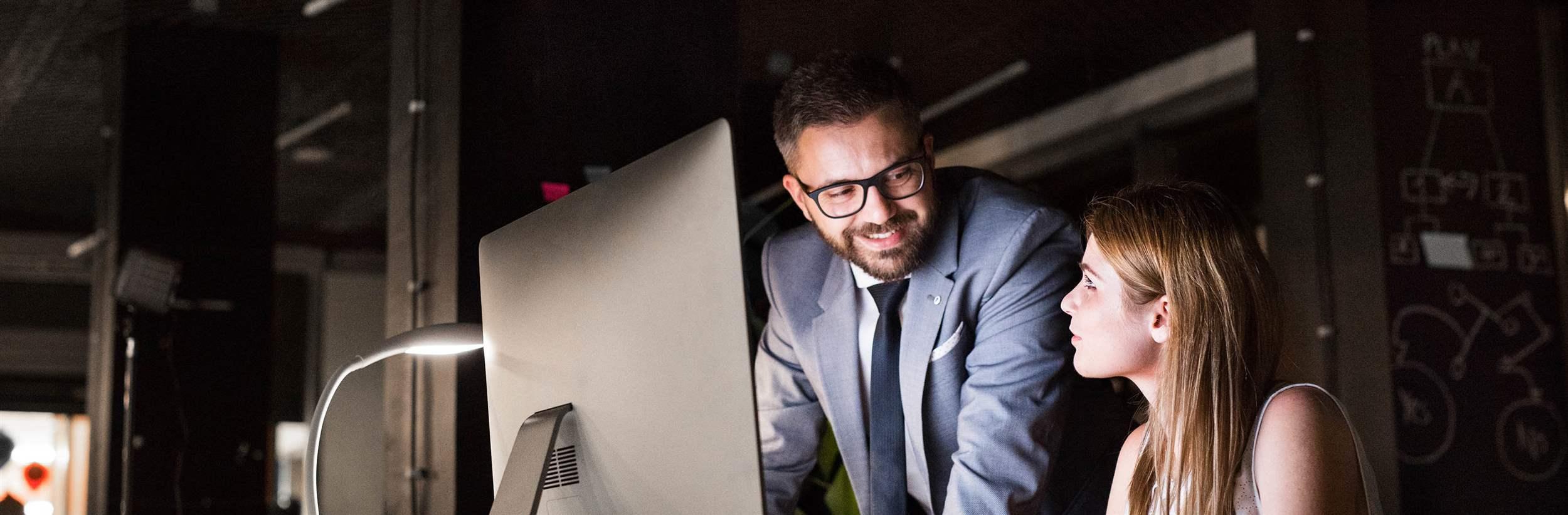 Two young businesspeople in the office at night working late, discussing a project.