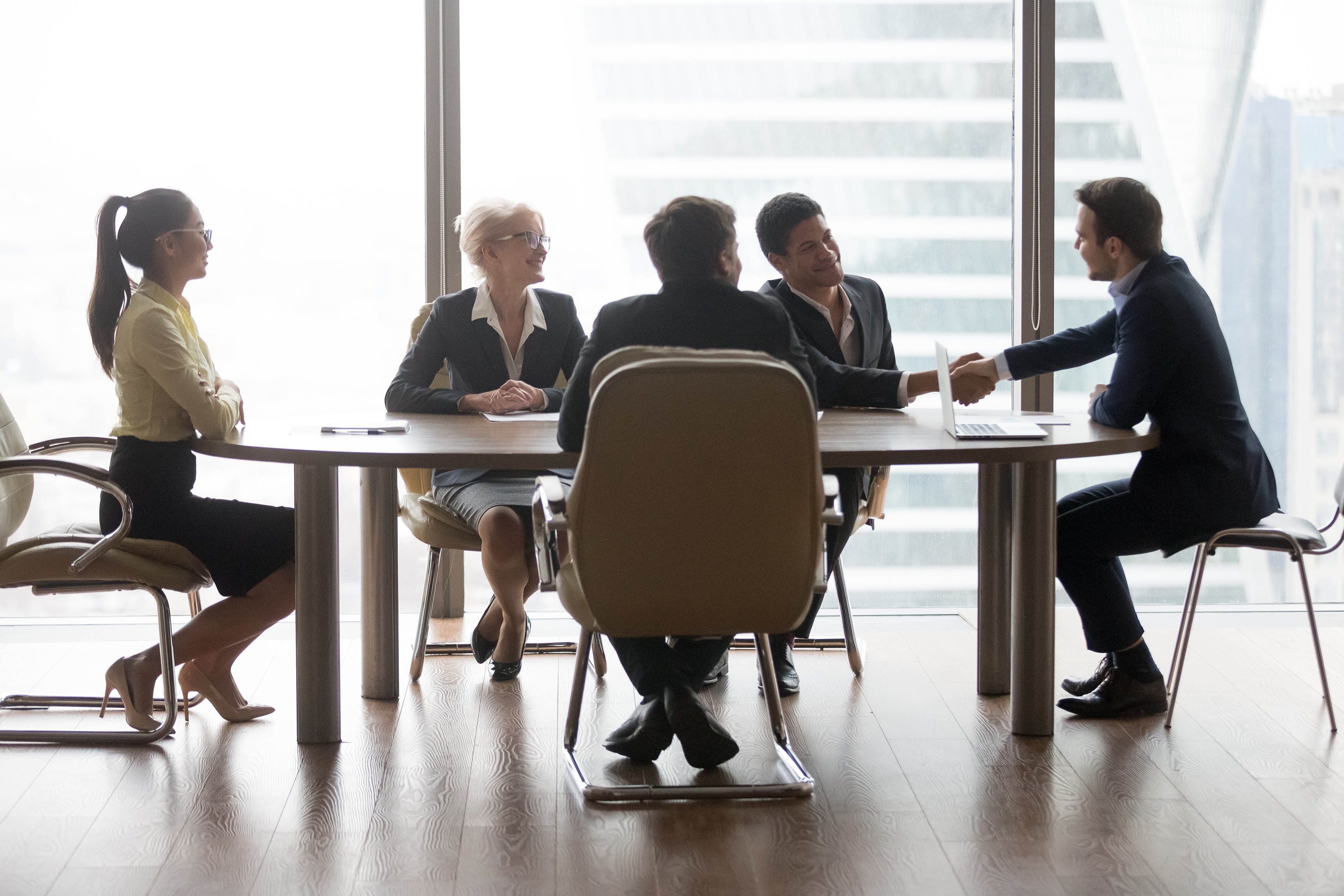 Smiling multiracial business people sitting at meeting in conference room and handshake. 