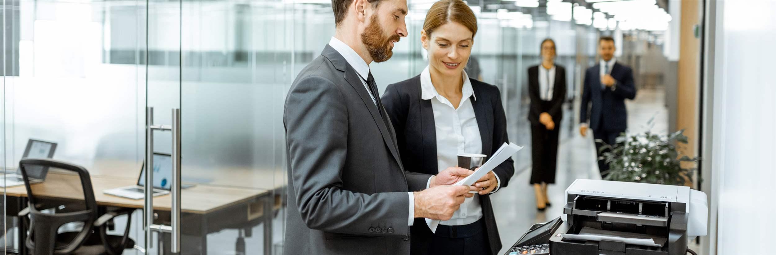Business man and woman talking near the copier during a coffee break in the hallway of the big corporation