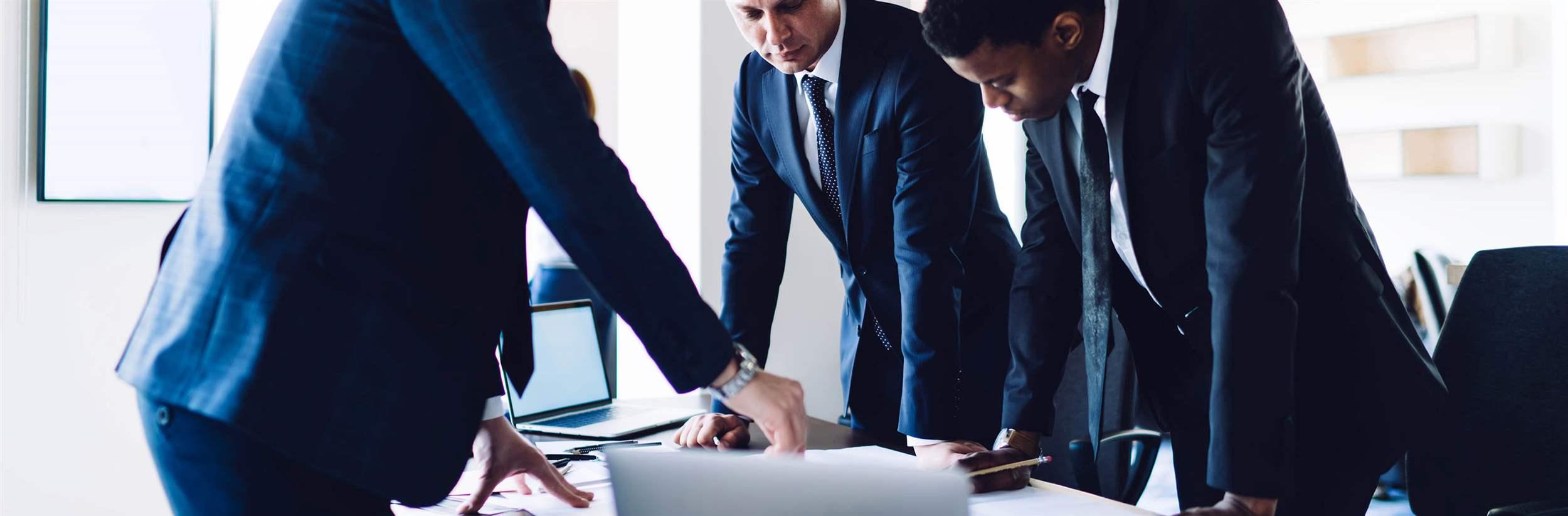 Side view of successful businessman explaining and sharing business ideas to multiracial focused colleagues while standing at desk during meeting in office room