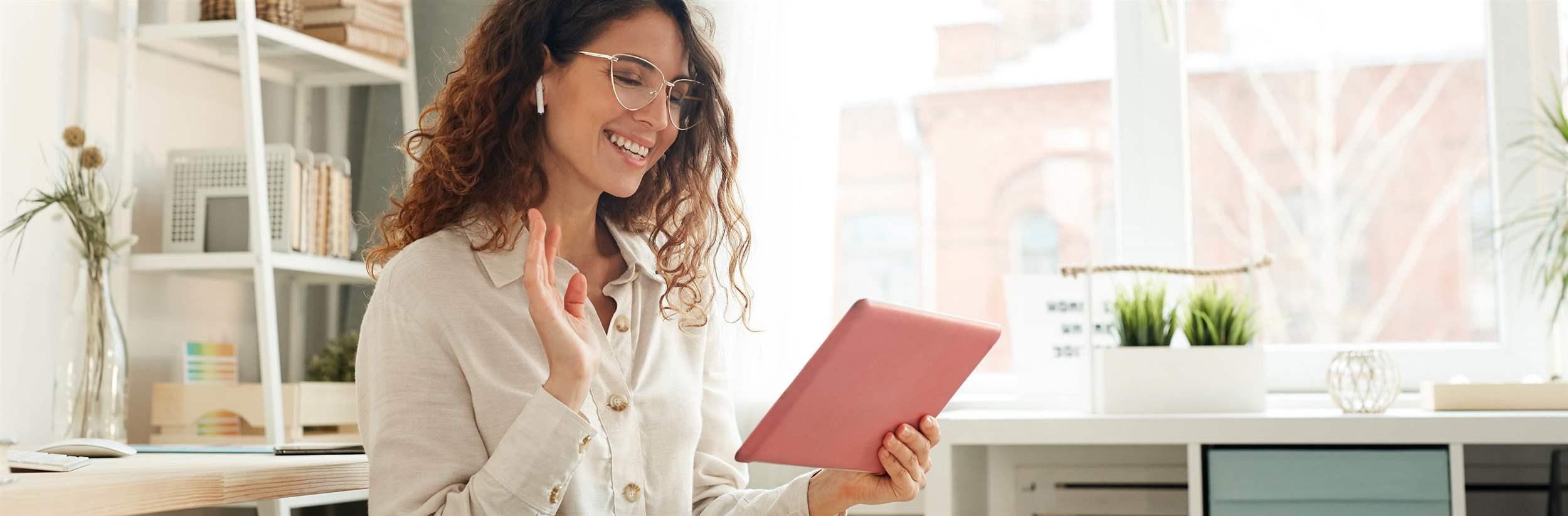 Une jeune femme moderne habillée de façon élégante participe à une vidéoconférence avec ses collègues de travail depuis son domicile.