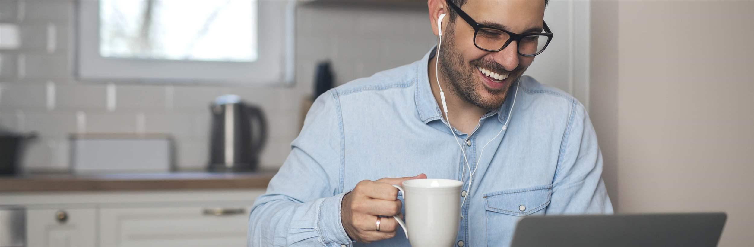 Young man drink coffee while wearing earphones and having a video call on laptop.