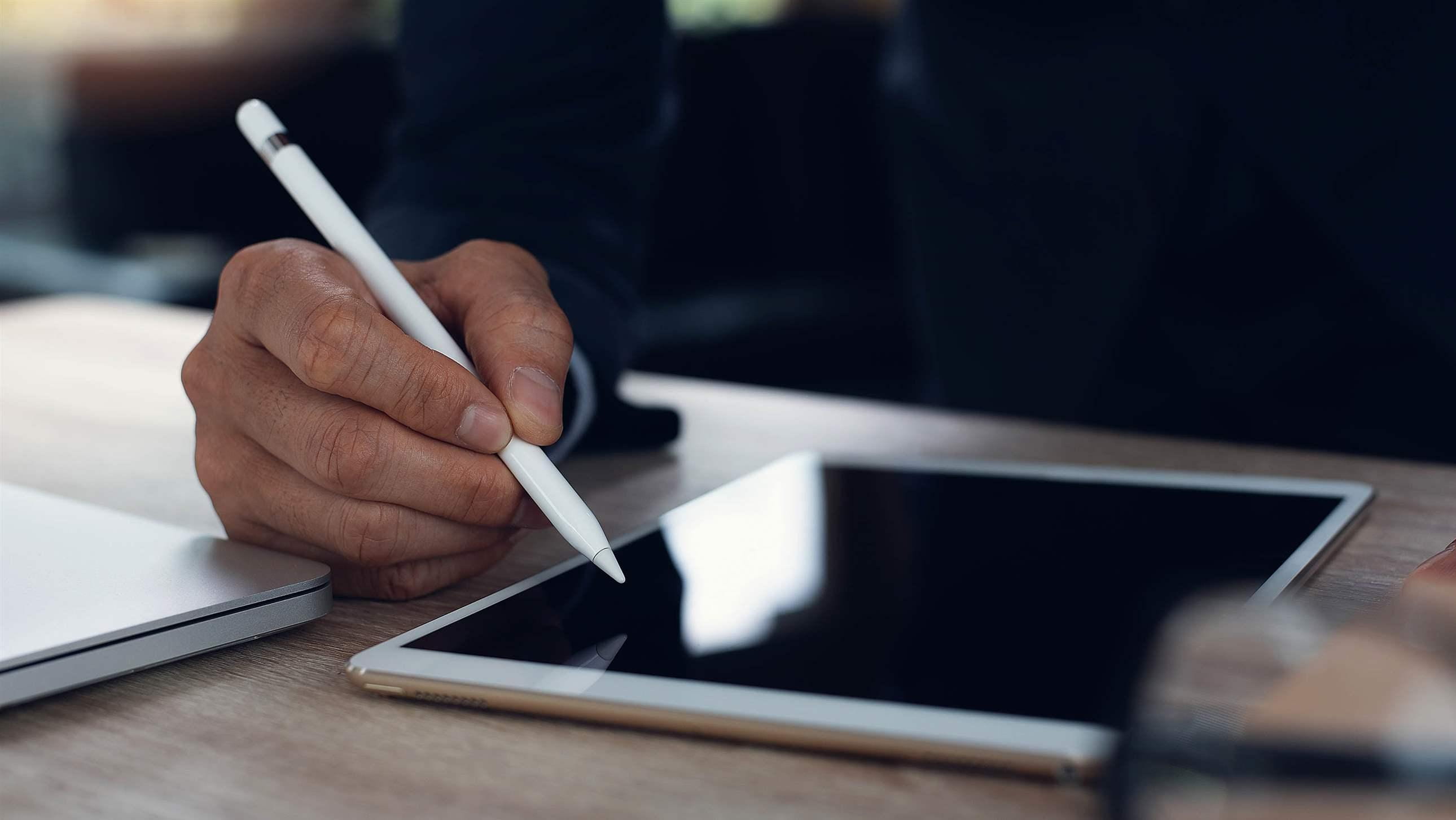 Businessman hand working with stylus pen on digital tablet with laptop computer on wooden desk in modern office, close up. Man messaging on tablet pc via mobile apps. Business plan, electronic signature concept