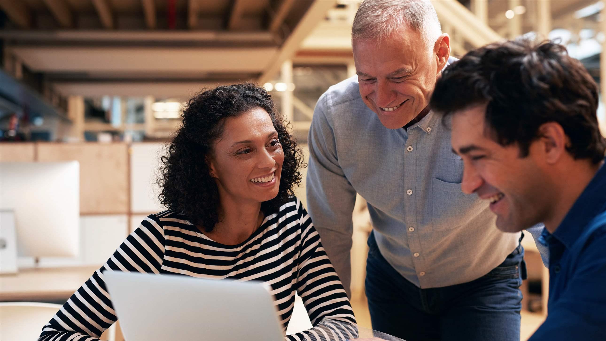 Diverse group of casually dressed smiling professional colleagues talking together over a laptop while having a meeting at a desk in a modern office