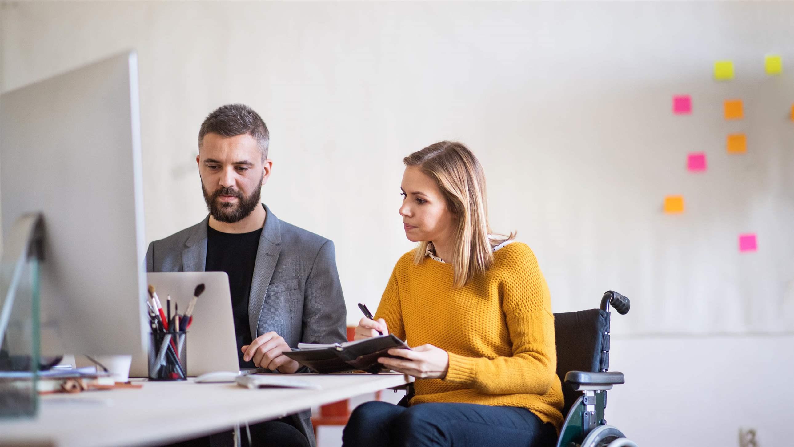 Two business people in the office working together. A man and woman in a wheelchair consulting a project.
