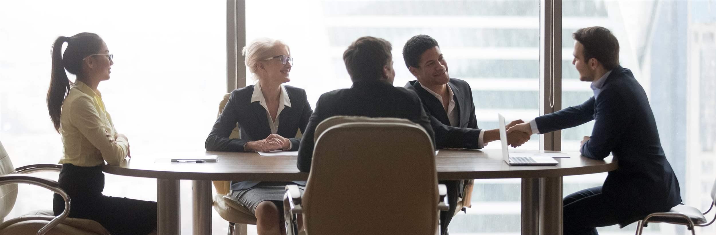 Smiling multiracial business people sitting at meeting in conference room and handshake.