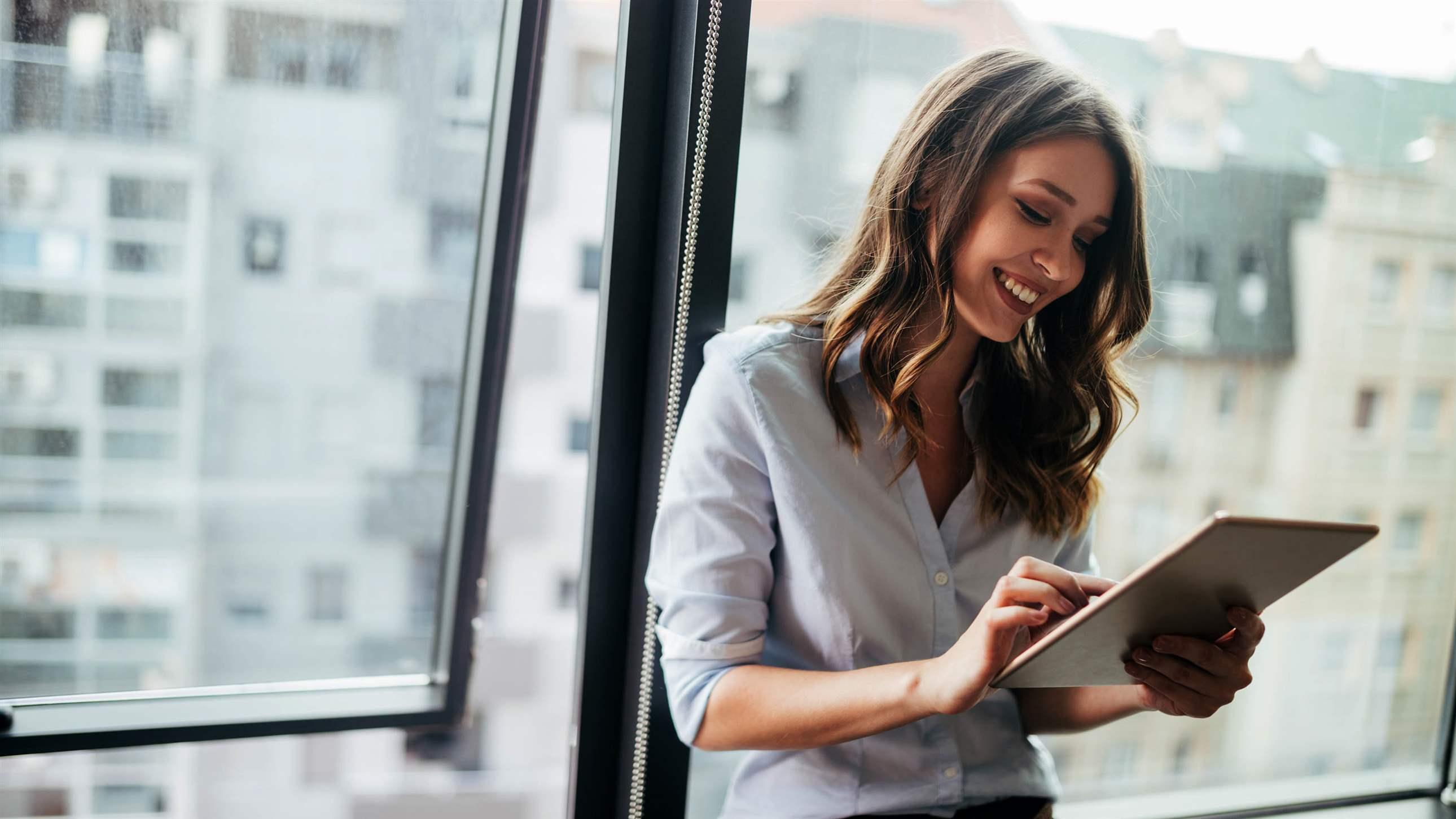 Young businesswoman using a digital tablet while standing in front of windows in office