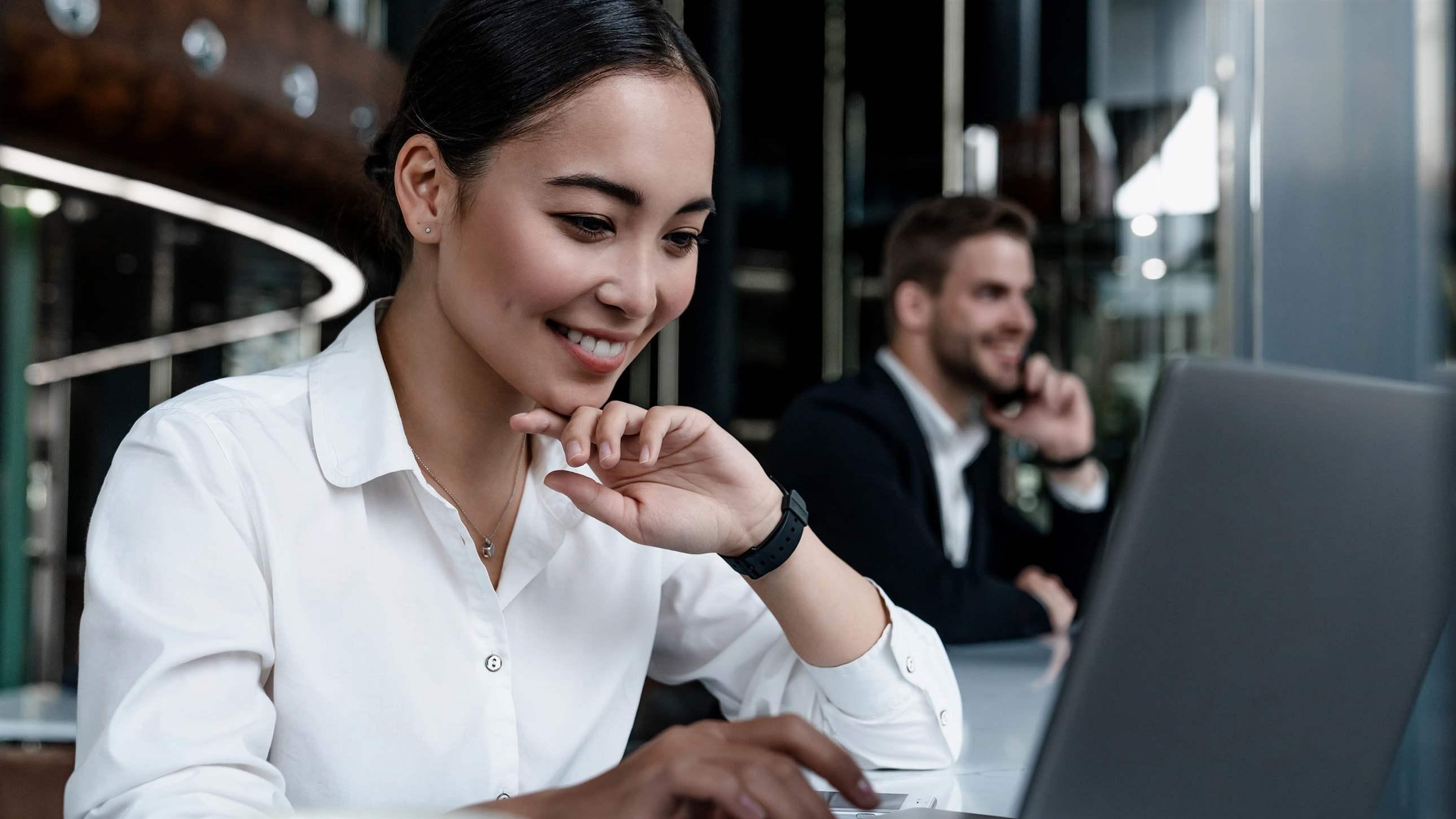 Smiling woman sitting at cafe working at laptop on table with coffee cup on it