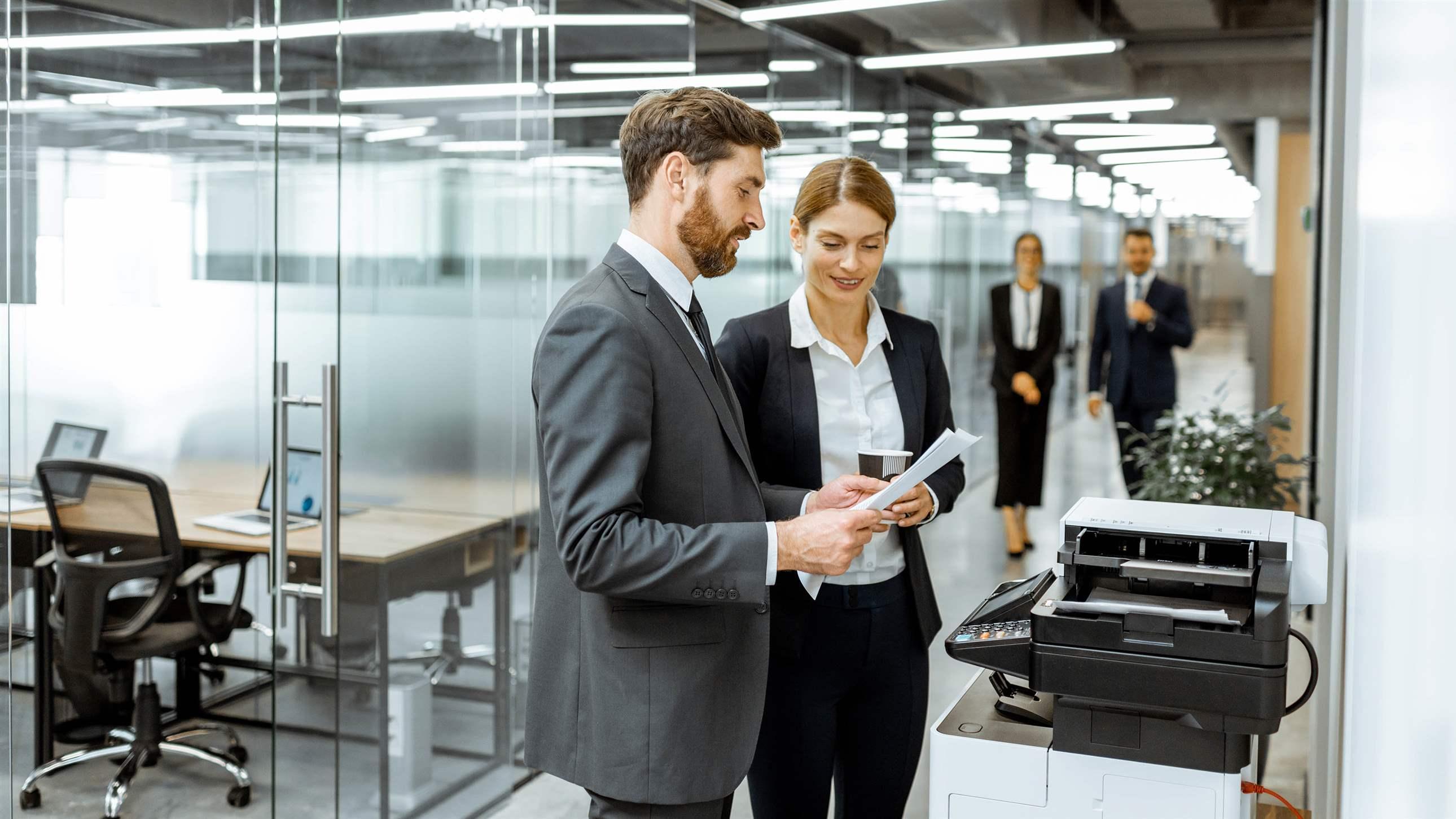 Business man and woman talking near the copier during a coffee break in the hallway of the big corporation