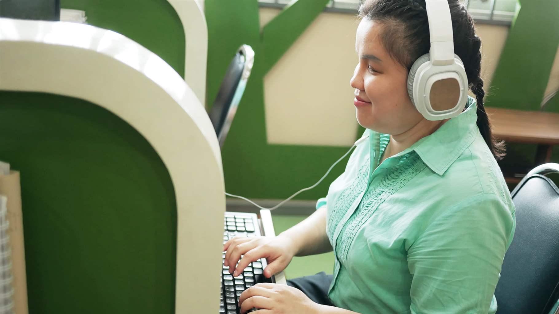 Blind woman in headphone typing on computer keyboard